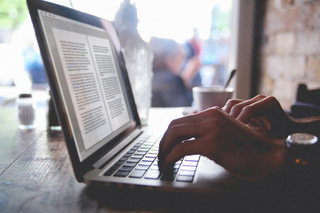 Vintage toned image of man's hands typing on the laptop in the cafe. Finishing a written work, novel or a book while drinking coffee.